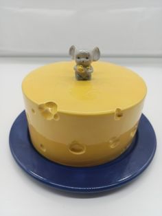 a yellow and blue cake with a little mouse on it's top sitting on a plate