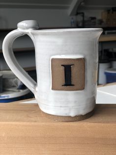 a ceramic mug with the letter i on it is sitting on a wooden table in a kitchen