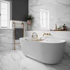 a white bath tub sitting next to a window in a bathroom with marble walls and floors