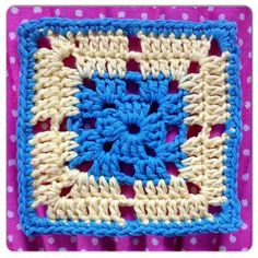 a crocheted square with blue and white squares in the center on a pink background