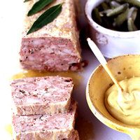 sliced meatloaf with mustard and green beans on a white plate next to a small bowl