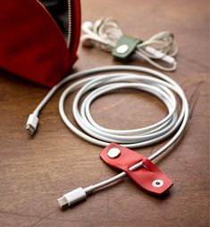 a red case sitting on top of a wooden table next to a charger and wires