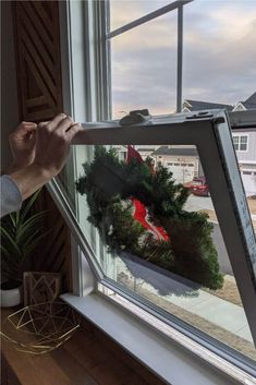 a person is holding up a window with a wreath on the outside and inside it