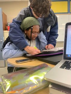 two people looking at a laptop on a table in front of an open book bag