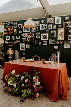 an orange table cloth with flowers and vases on it in front of a green wall