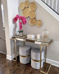 a console table with two stools and a vase on it in front of a staircase