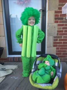 a child in a green costume standing next to a baby in a stroller