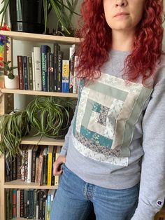 a woman with red hair standing in front of a bookshelf filled with plants