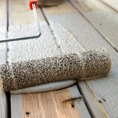 a close up of a paint roller on the floor with wood planks and cement