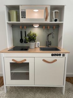 a white kitchen with a sink and cupboards on the wall above it is also a potted plant