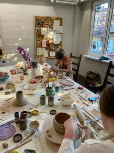 two women sitting at a table making vases with paint and paper on the table