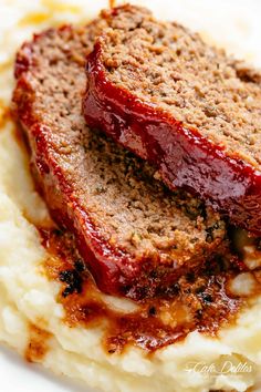 two slices of meatloaf on top of mashed potatoes with ketchup