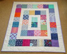 a multicolored patchwork quilt on the floor with a square in the center