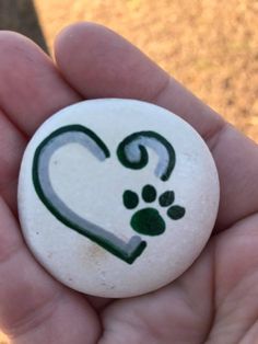 a hand holding a white rock with a green heart and paw prints on it's side