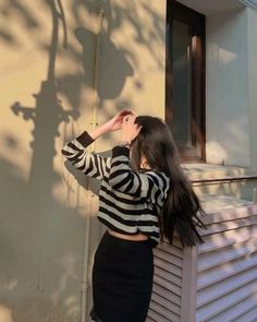 a woman standing next to a building with her hair blowing in the wind while wearing a black and white striped top