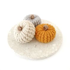 two crocheted pumpkins sitting on top of a white plate next to each other