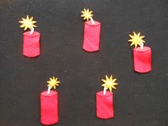 four red candles with yellow stars on them sitting in the middle of a black surface