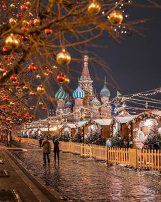 two people walking down the street in front of christmas decorations and buildings with lights on them