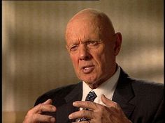 an older man wearing a suit and tie talking to someone in front of the camera