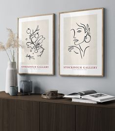 two framed art prints on the wall above a wooden cabinet with vases and books