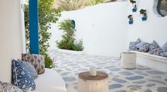 an outdoor seating area with blue and white pillows on the floor, potted trees in the background