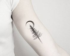 a woman's arm with a pine tree and crescent tattoo on the left forearm