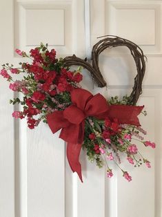 a heart shaped wreath with red flowers and greenery on the front door for valentine's day