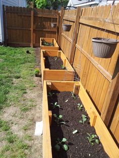 several wooden planters filled with dirt and plants in the back yard, next to a fence