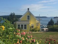 a yellow house sitting on top of a lush green field next to the ocean with boats in the water