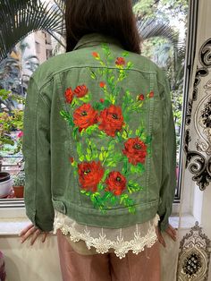 a woman standing in front of a window wearing a green jacket with red flowers on it