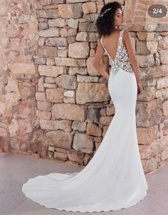 a woman standing in front of a stone wall wearing a wedding dress with an open back