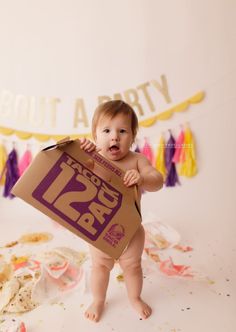 a baby holding up a brown paper bag with the number 12 on it's chest