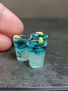 two glasses filled with blue liquid and lemon slices on top of a table next to a hand