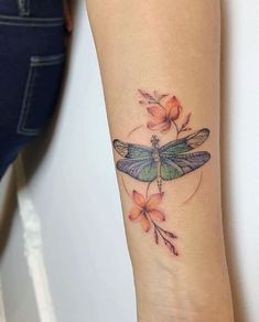 a woman's arm with a dragonfly tattoo on it and flowers in the background