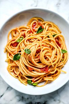 a white bowl filled with pasta and sauce on top of a marble countertop next to a fork