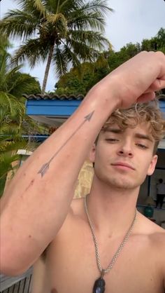 a shirtless young man holding his arm up to his head with palm trees in the background