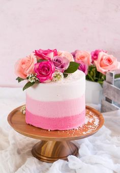 a cake with pink and white frosting on a wooden plate next to some flowers