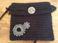 a black crocheted purse with a button on it sitting on top of a wooden table