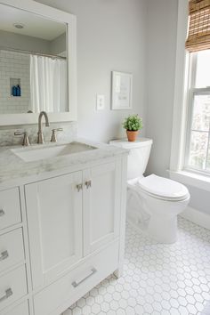 a white bathroom with a toilet, sink and window in the corner by the tub