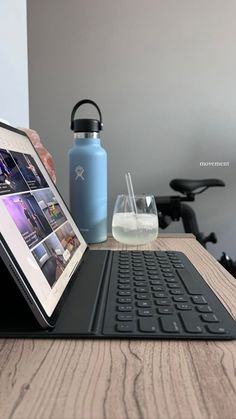 an open laptop computer sitting on top of a wooden table next to a drink bottle