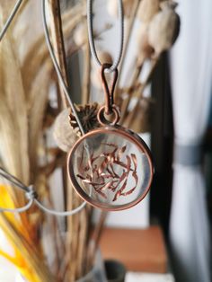 dried flowers in a glass vase with a metal necklace hanging from it's side