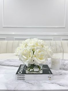 white roses in a glass vase on top of a stack of chandelier books