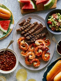 an assortment of food on a table with watermelon slices, beans and hot dogs