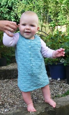 a baby in a blue knitted dress is being held by someone's hand