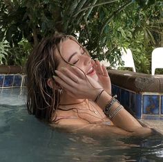 a woman laying in the water with her hands on her face and eyes closed, smiling