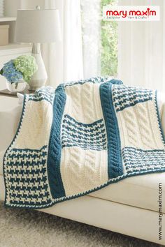 a white couch sitting next to a window covered in a blue and white crocheted blanket