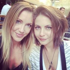 two beautiful young women sitting next to each other in front of a table with people