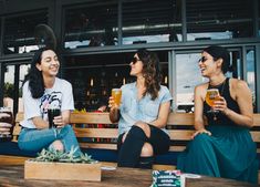 three women are sitting on a bench drinking beer and laughing at each other while another woman sits next to them