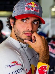 a man in a red bull hat listening to ear buds and looking at the camera