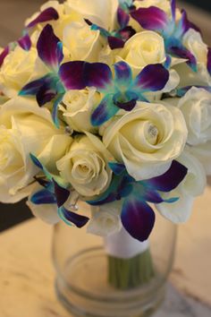 a bouquet of white roses and purple orchids in a glass vase on a table